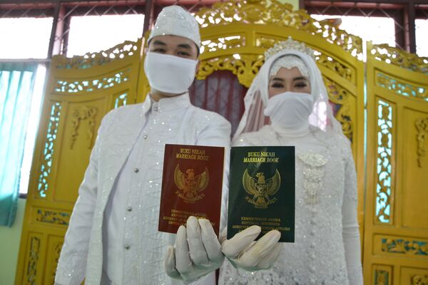 Groom Dwi Pradipta (L) and bride Siti Nurjanah (R) hold up their marriage books, or certificates, after a wedding ceremony while wearing face masks amid the COVID-19 coronavirus outbreak in Jakarta on April 5, 2020.  - Sputnik Казахстан