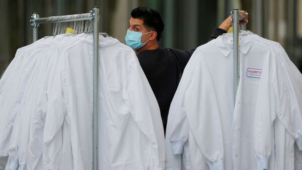 Мужчина в маске двигает стойки с защитными костюмами в лаборатории, где разрабатывают вакцину для борьбы с коронавирусом  - Sputnik Қазақстан
