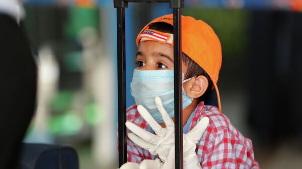 Ребенок в защитной маске и перчатках опирается на чемодан в ожидании рейса - Sputnik Қазақстан