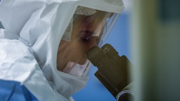 Сотрудник лаборатории в защитном костюме изучает образцы коронавируса под микроскопом - Sputnik Казахстан