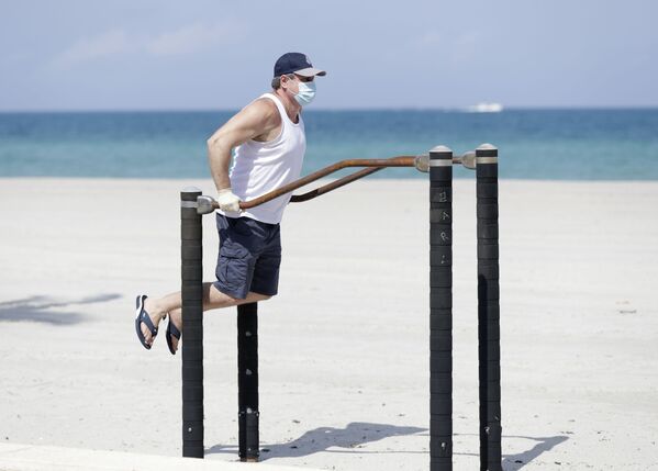 Мужчина в защитной маске во время выполнения упражнений на турнике на пляже в Голливуде, США - Sputnik Казахстан