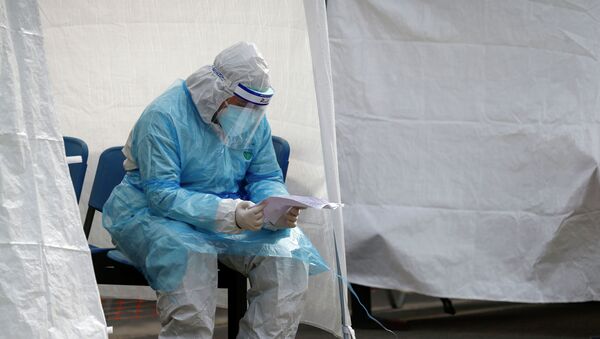 Медик в защитном костюме изучает документы в ожидании пациентов с коронавирусом - Sputnik Казахстан
