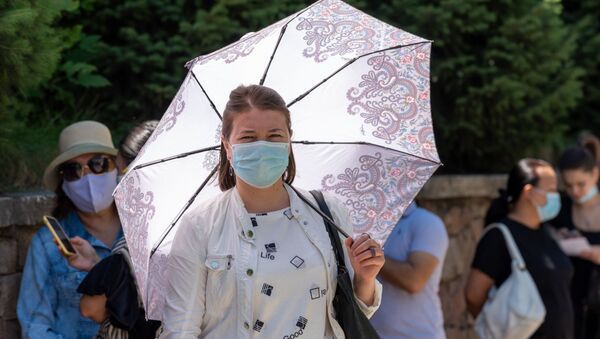 Женщина в маске под зонтом стоит в очереди перед центральной аптекой в Алматы  - Sputnik Қазақстан