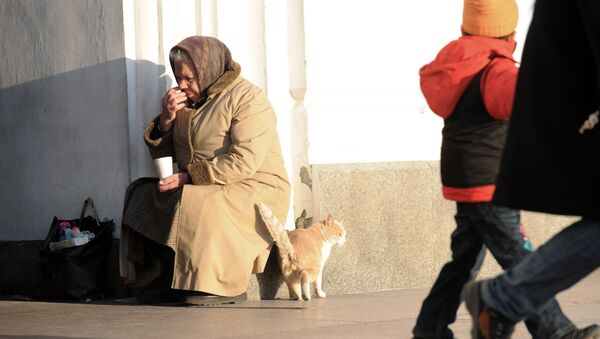 Бездомная кошка трется о ноги пожилой женщины, занимающейся попрошайничеством на улице - Sputnik Казахстан