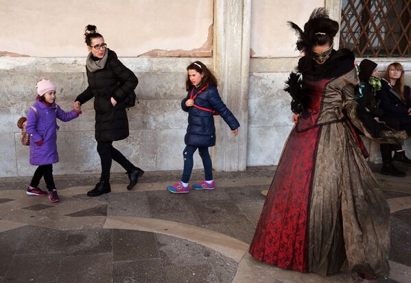 Женщина с детьми проходят мимо участницы Венецианского карнавала в день его открытия - Sputnik Казахстан