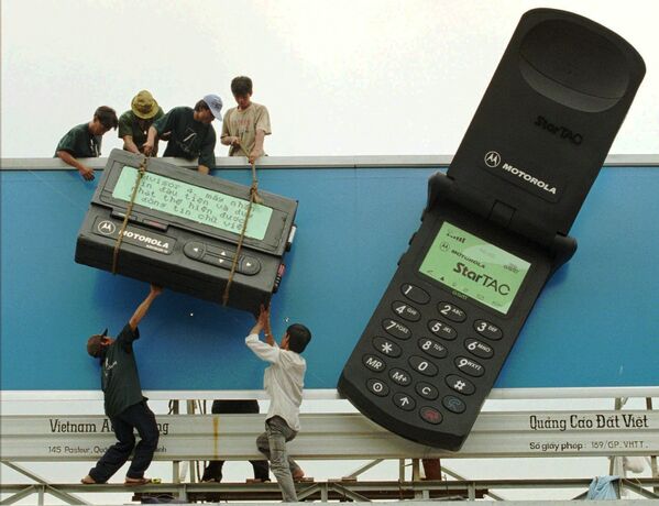Рабочие размещают гигантские макеты пейджера и мобильного телефона с рекламой телекоммуникационных продуктов Motorola в городе Хошимин, 1996 - Sputnik Казахстан